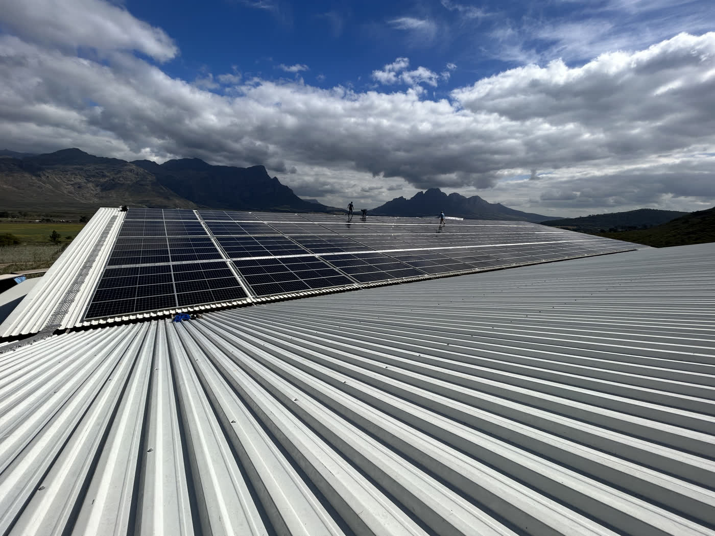 Installers fitting solar panels on a commercial roof, mountains in the background