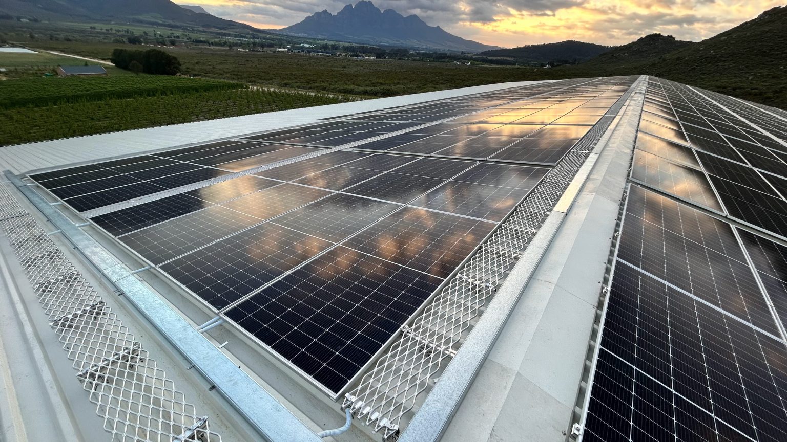 Completed 480kWp commercial rooftop solar PV array at dusk, with vineyards and mountains behind